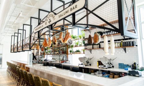 Designed to resemble a brasserie, white tile with a black stripe accent adorns the wall behind the mozzarella bar. The bar
die wall is covered in a textured, dimensional cracked roman look in a muted palette.